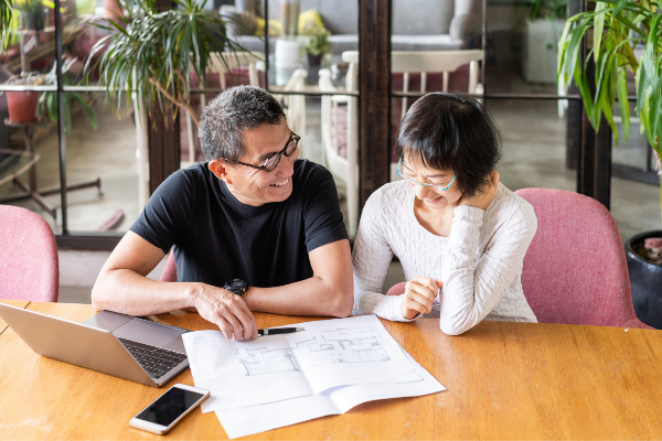 Older Asian couple smiling while reviewing plans for their home renovation.