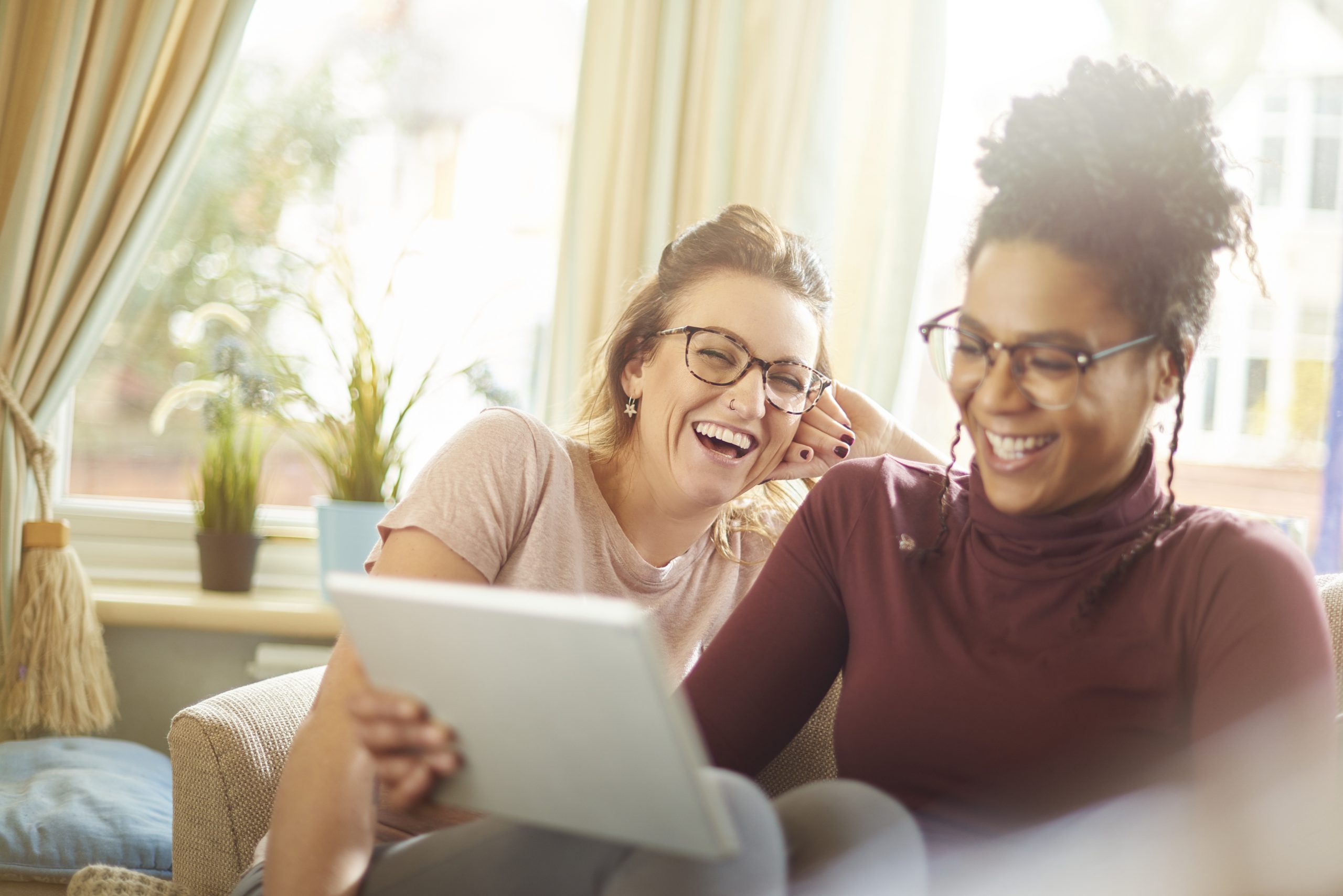 a female same sex couple sit on the sofa on their digital tablet