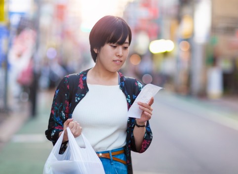 Young Asian woman walking down street holding a shopping bag and checking her receipt