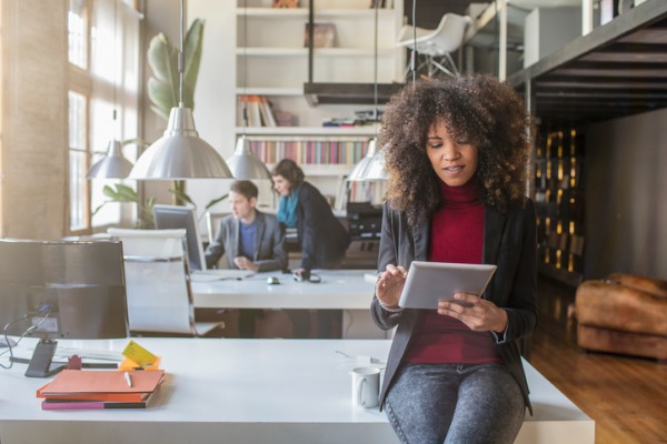 Woman working with the digital tablet in the office, her colleagues are talking in the background.