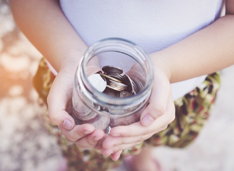 Small child's hands holding a jar full of coins