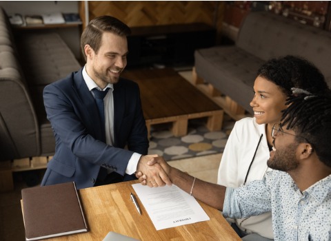 Happy biracial couple shaking hands with their realtor at a meeting.