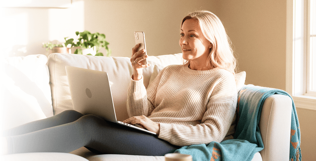 Woman relaxing on a couch at home using a laptop and smartphone